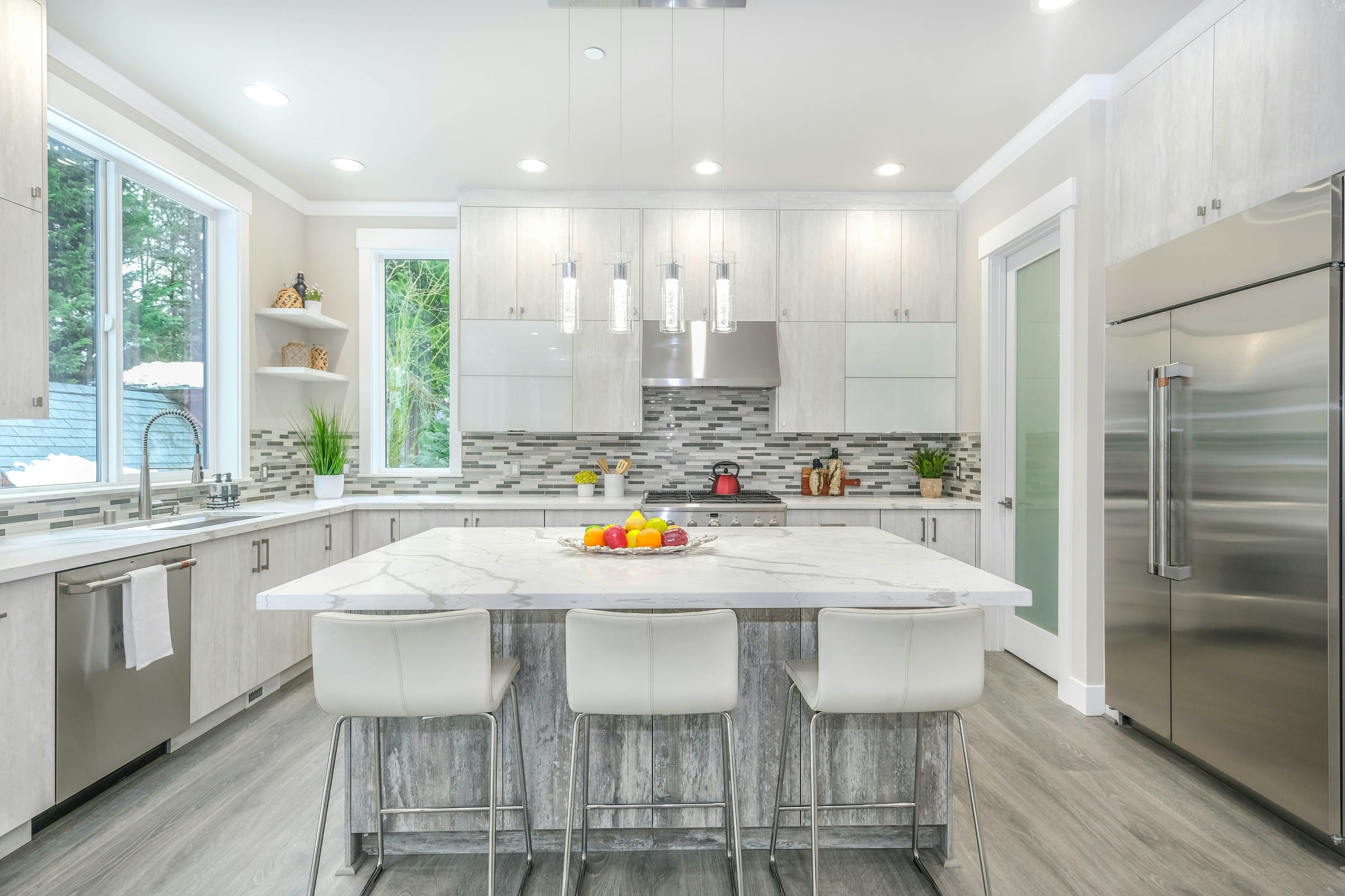 A spotless modern kitchen with white cabinets, a marble island, and pendant lights