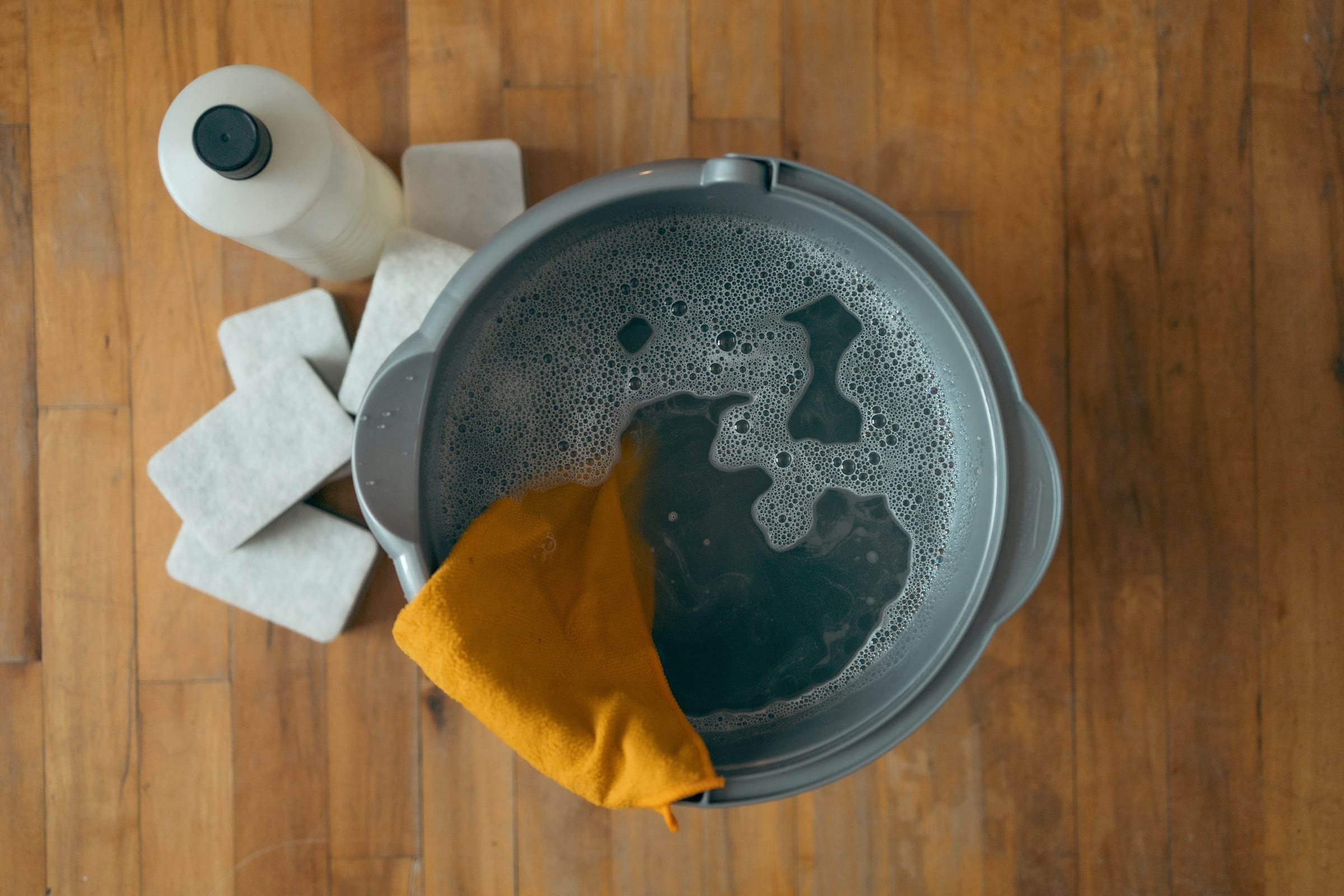 An overhead view of a mop bucket full of sudsy water with a yellow cloth draped over the rim
