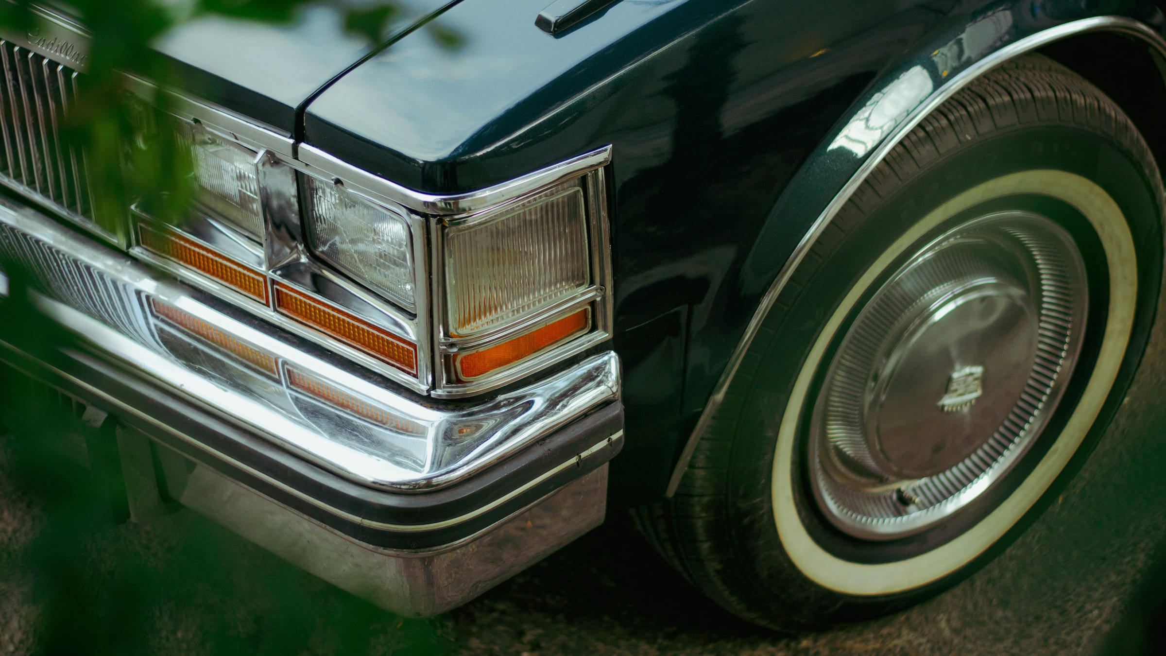 The chrome front end and whitewall tire of a gleaming vintage black Cadillac