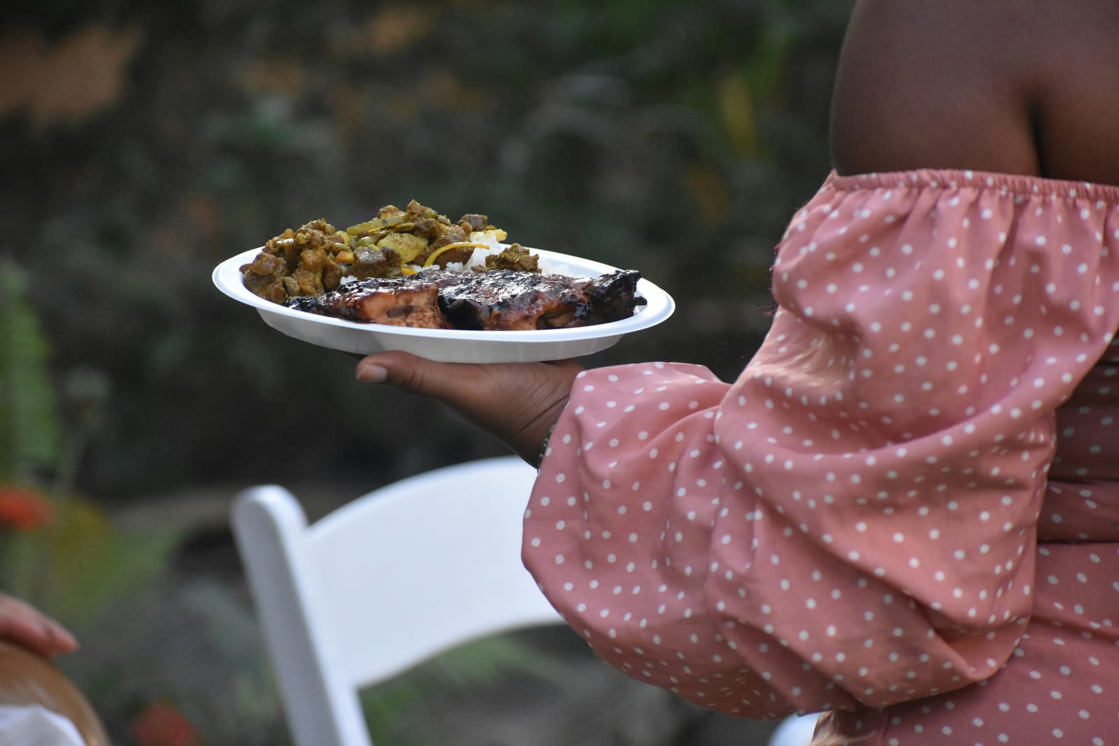 A plate of jerk chicken, curry, and rice held at an outdoor cookout gathering