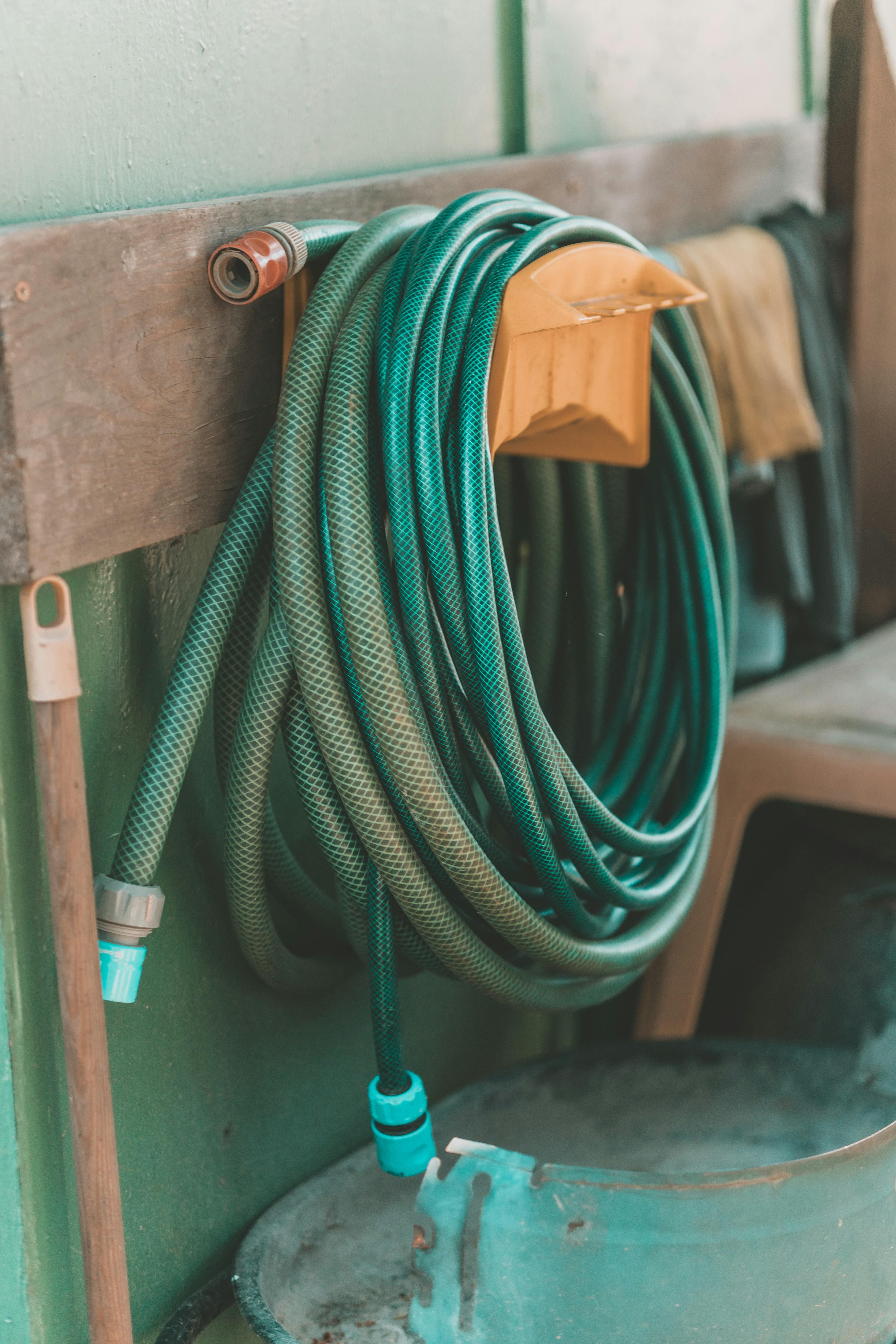A coiled green garden hose hanging on a wall-mounted holder