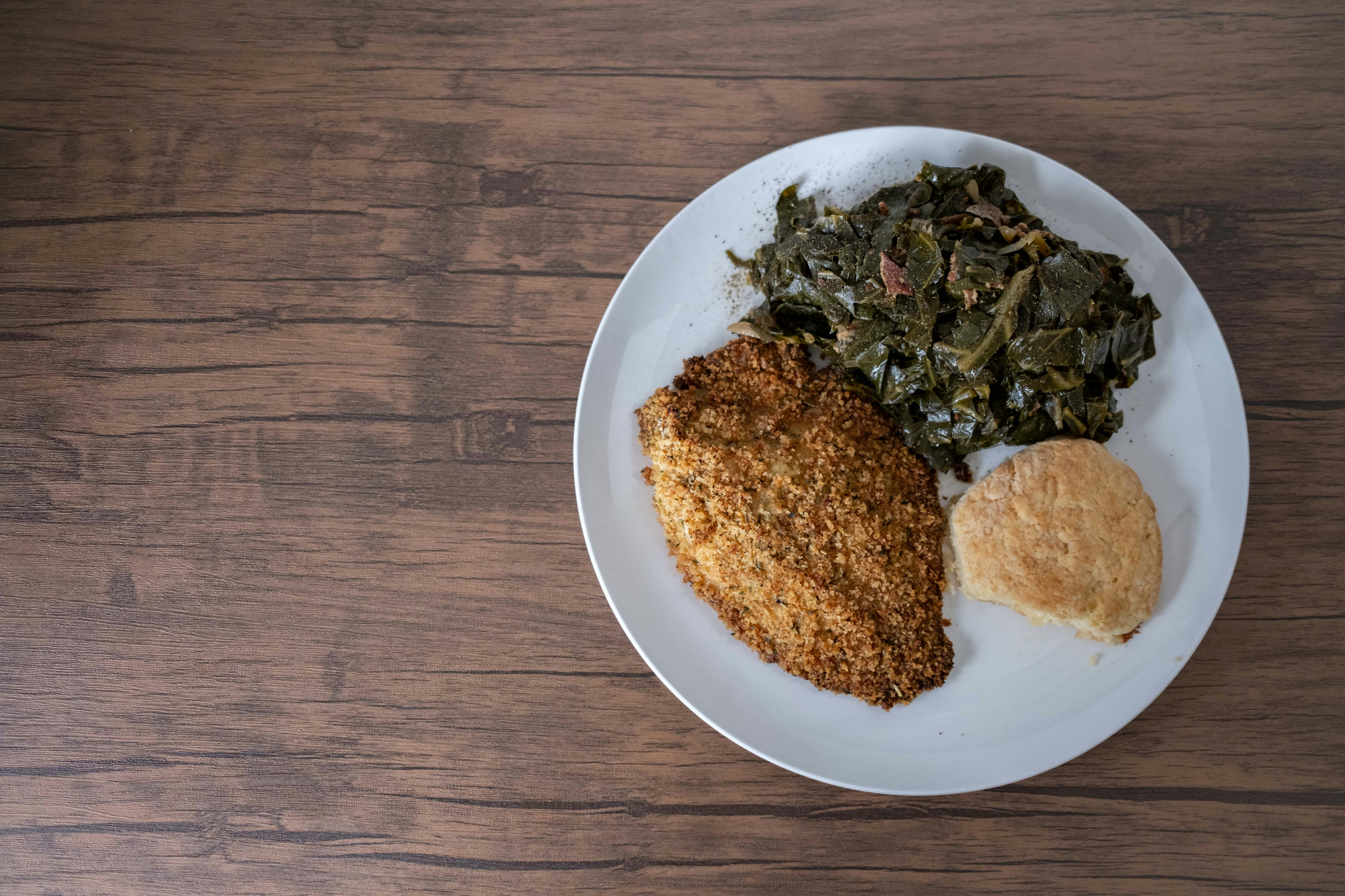 A soul food plate with fried fish, collard greens, and a biscuit